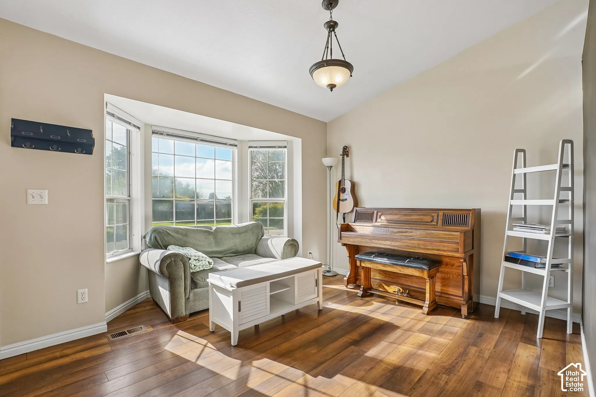 Living space featuring wood-finish flooring, vaulted ceilings, a multi-pane bay window, and a hanging pendant light fixture