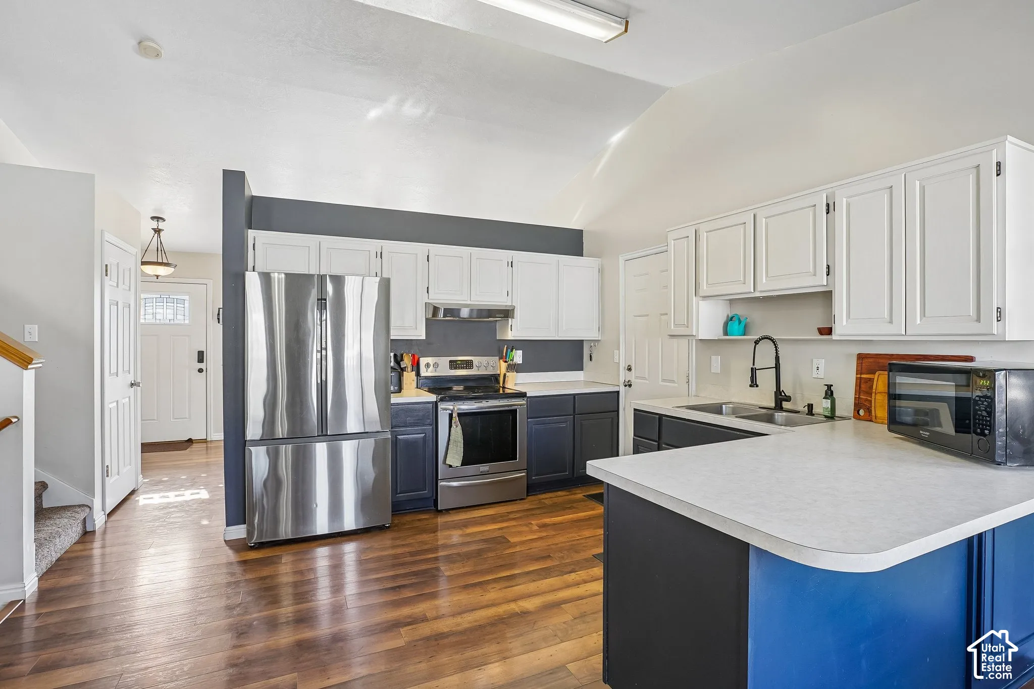 Kitchen featuring vaulted ceilings, wood-finish flooring, two-tone cabinetry, stainless steel appliances, and a matte black faucet