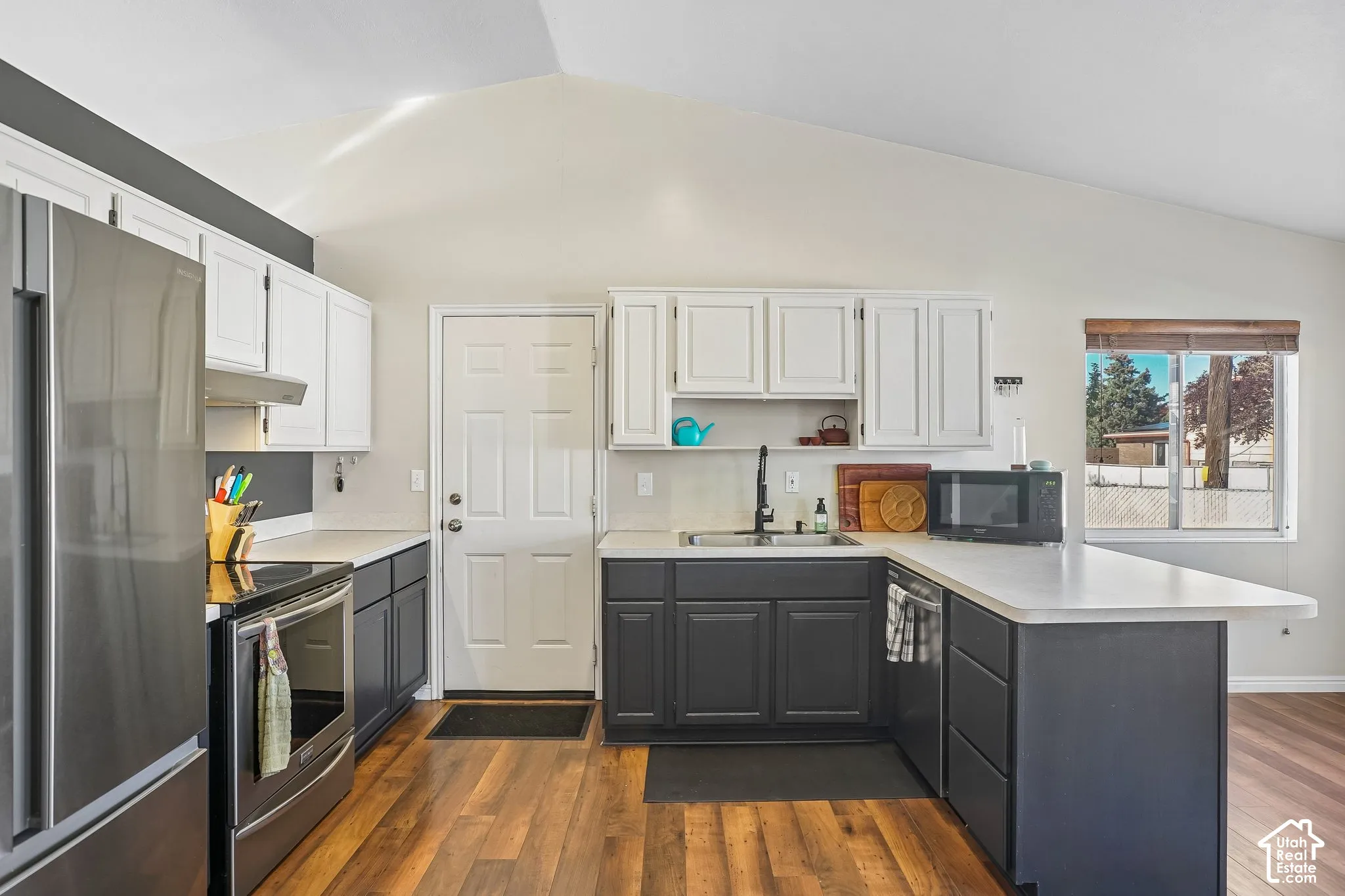 Kitchen featuring vaulted ceilings, two-tone cabinetry, wood-finish flooring, stainless steel appliances, and solid-surface countertops