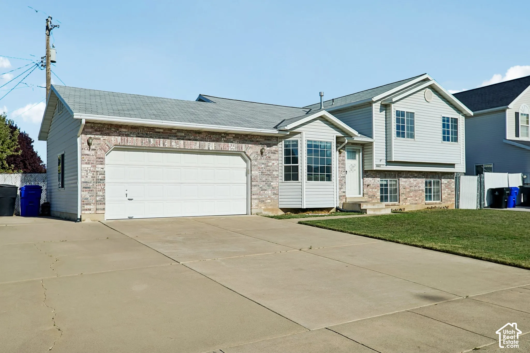 Split-level exterior featuring a multi-material facade of brick and horizontal siding, a bay window, an attached two-car garage, and an expansive concrete driveway