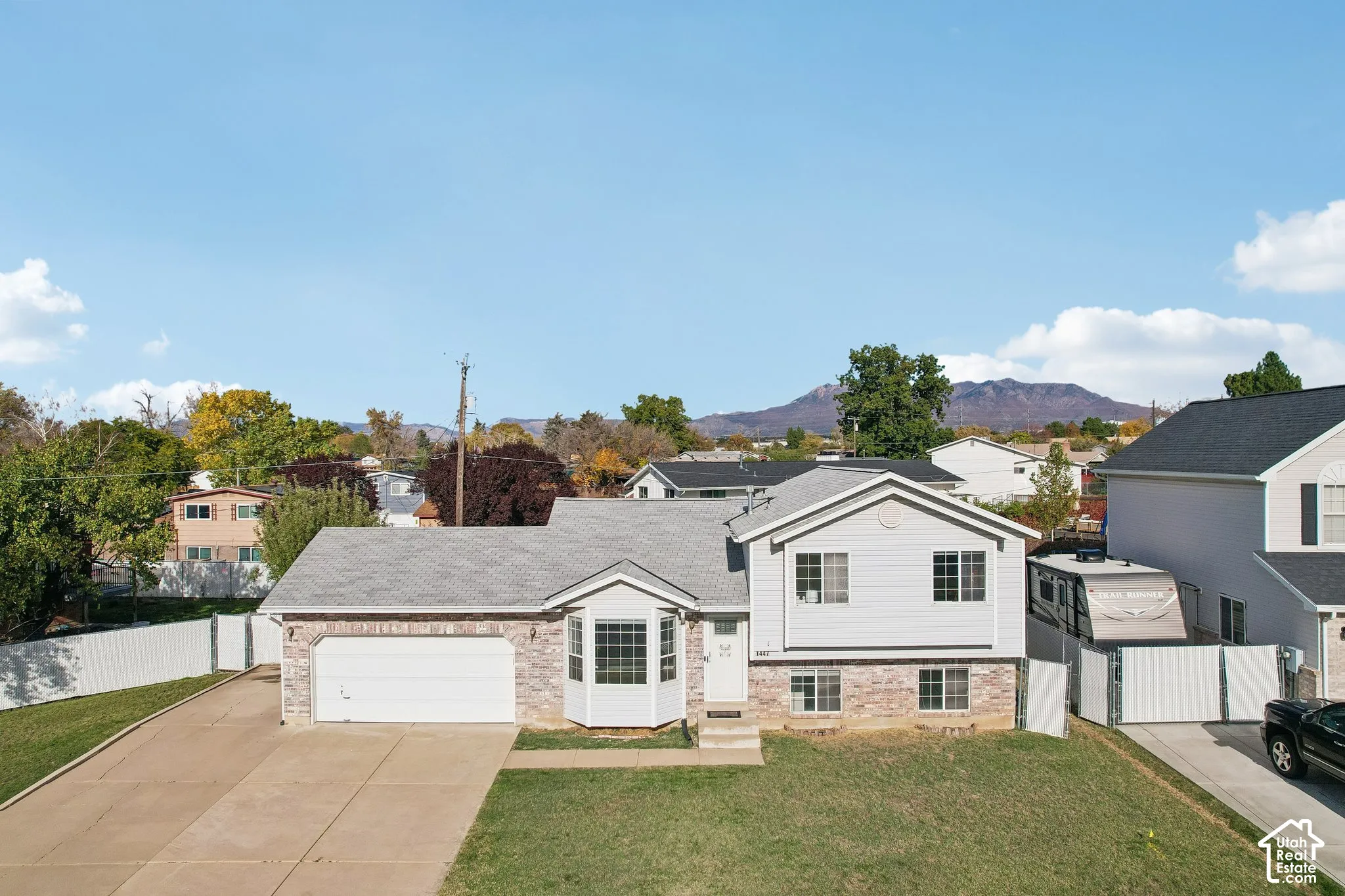 Split-level residence featuring a brick and horizontal siding exterior, attached two-car garage, bay window, concrete driveway, and mountain backdrop