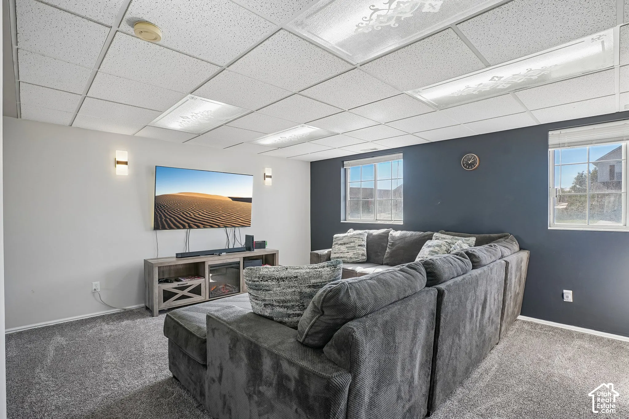 Finished interior space featuring a drop ceiling with integrated lighting, wall-to-wall carpeting, dual wall-mounted light fixtures, and a dual-tone wall finish