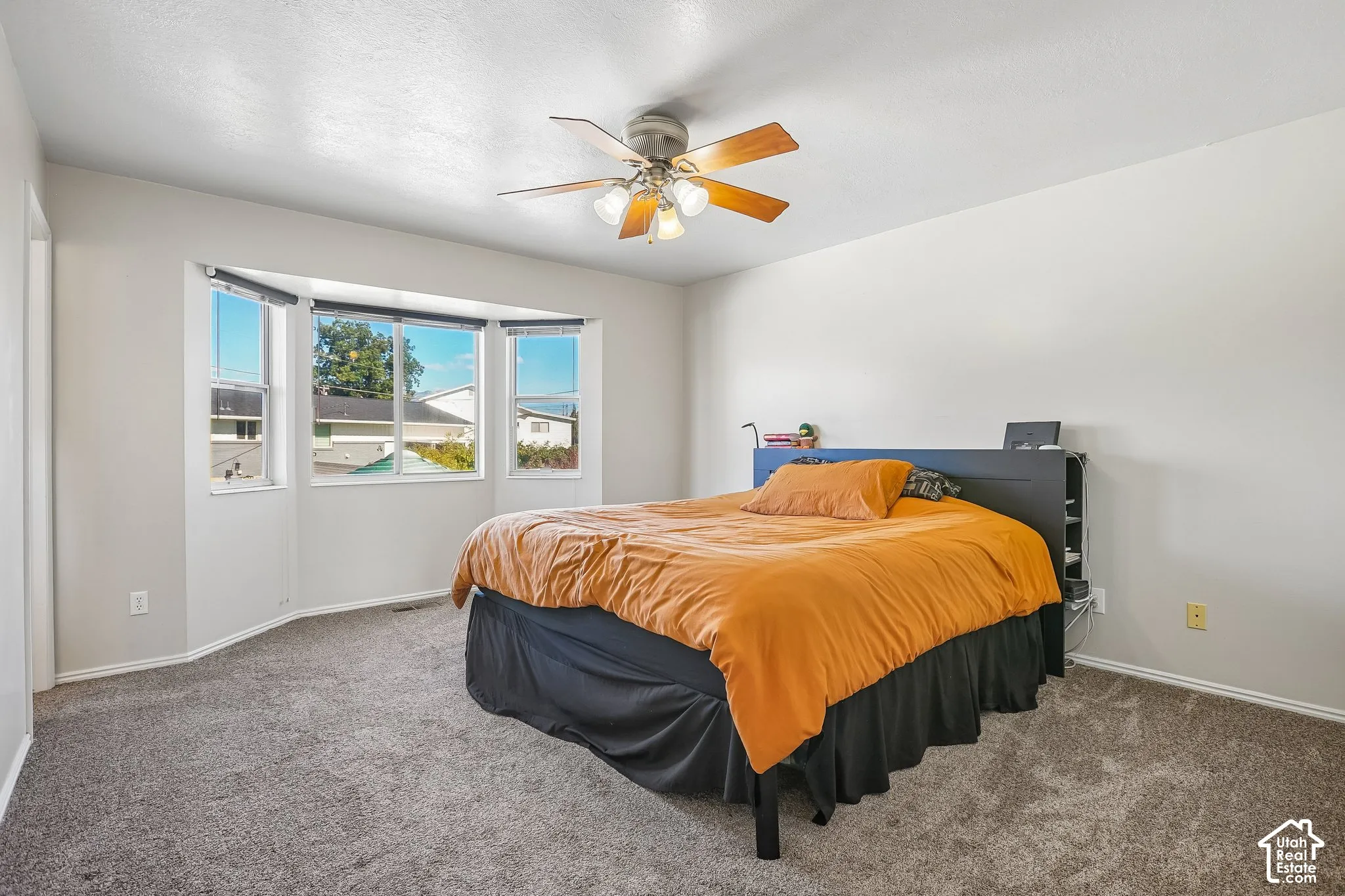 Bay window with multi-pane configuration, neutral carpeting, and ceiling fan with integrated light fixture