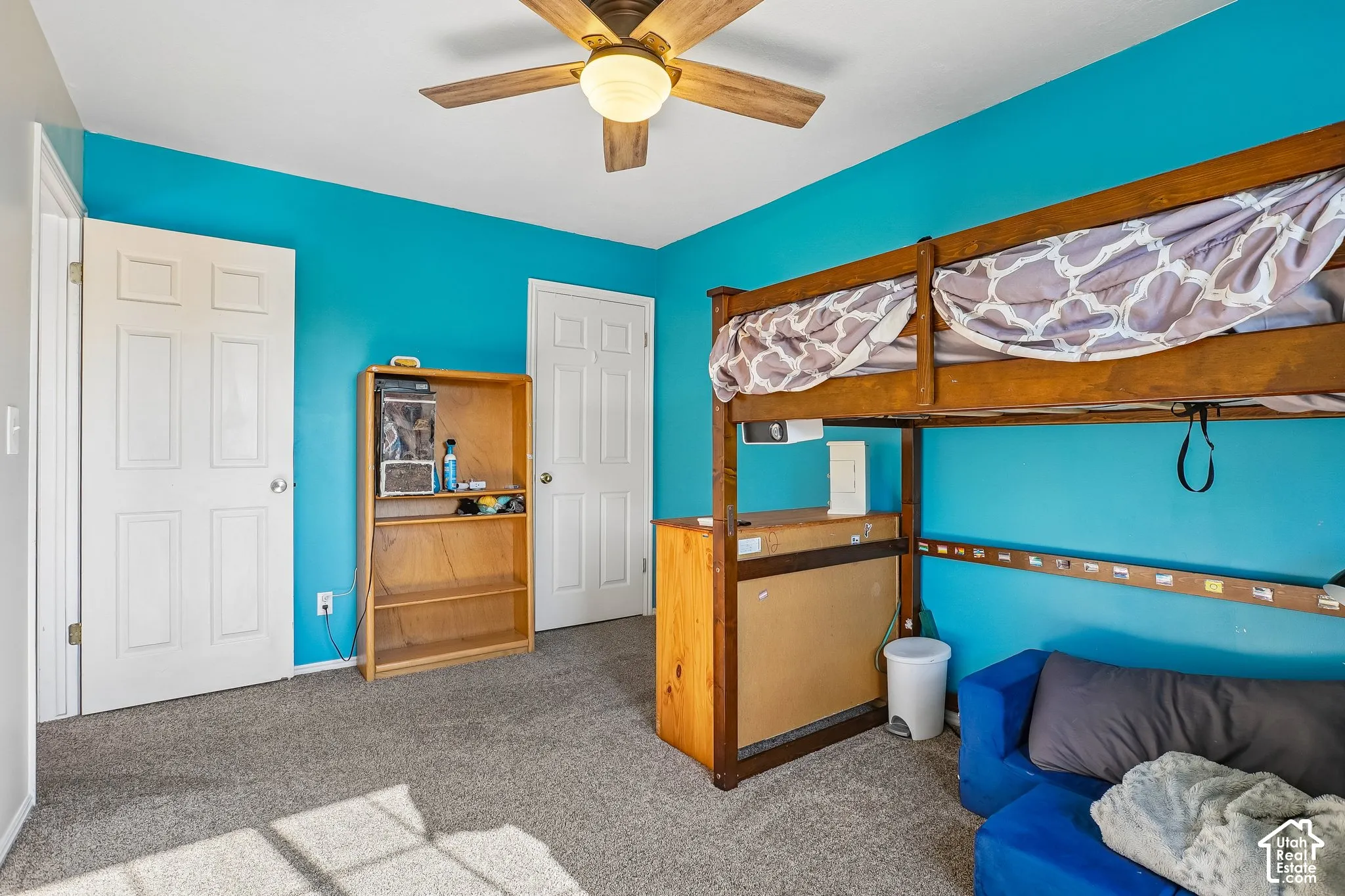 Bedroom featuring grey carpeting, two six-panel interior doors, and a ceiling fan with integrated lighting