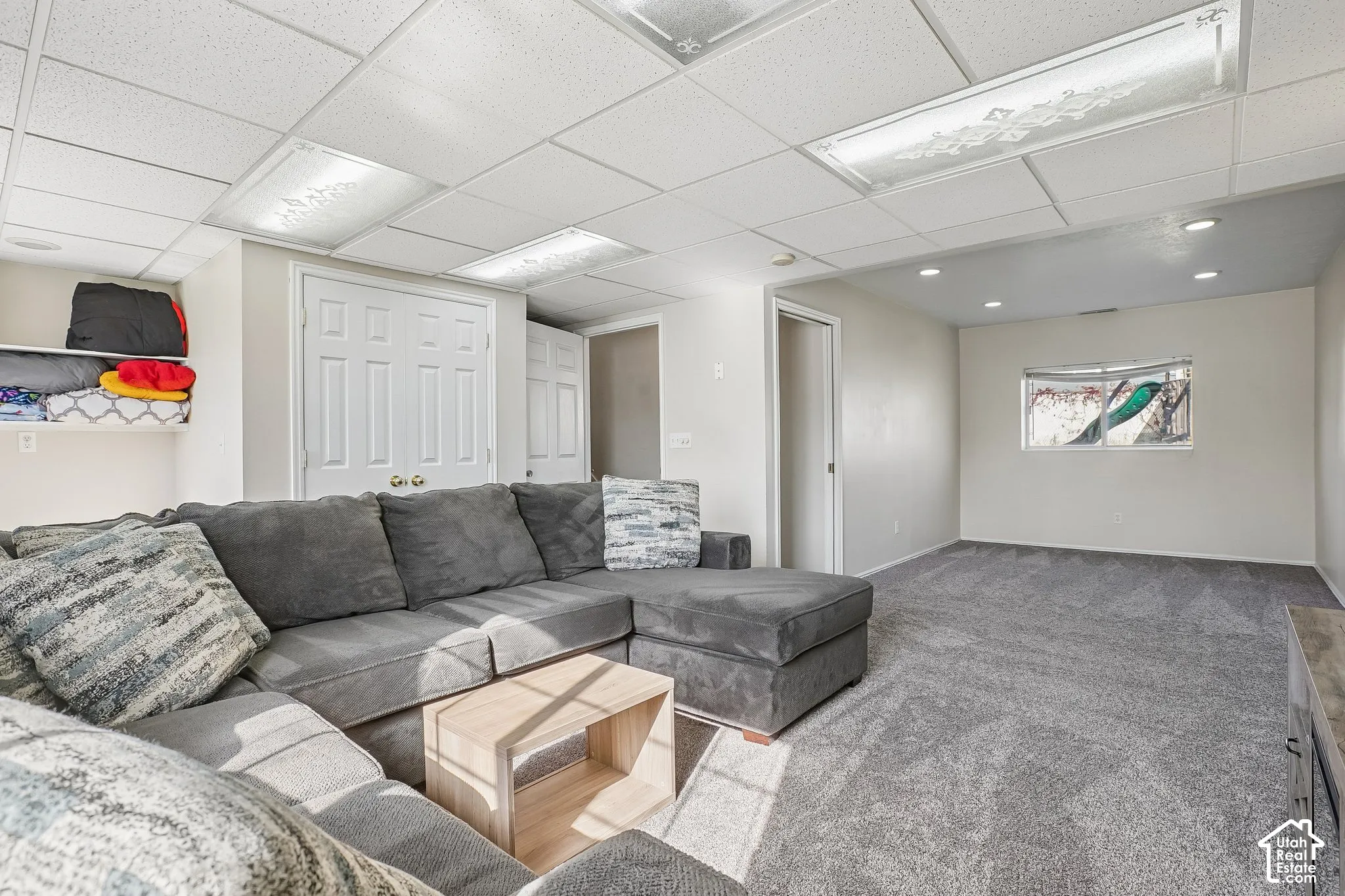 Neutral-toned interior space featuring recessed lighting, a drop ceiling with integrated rectangular light fixtures, carpeting, and double-door closet storage