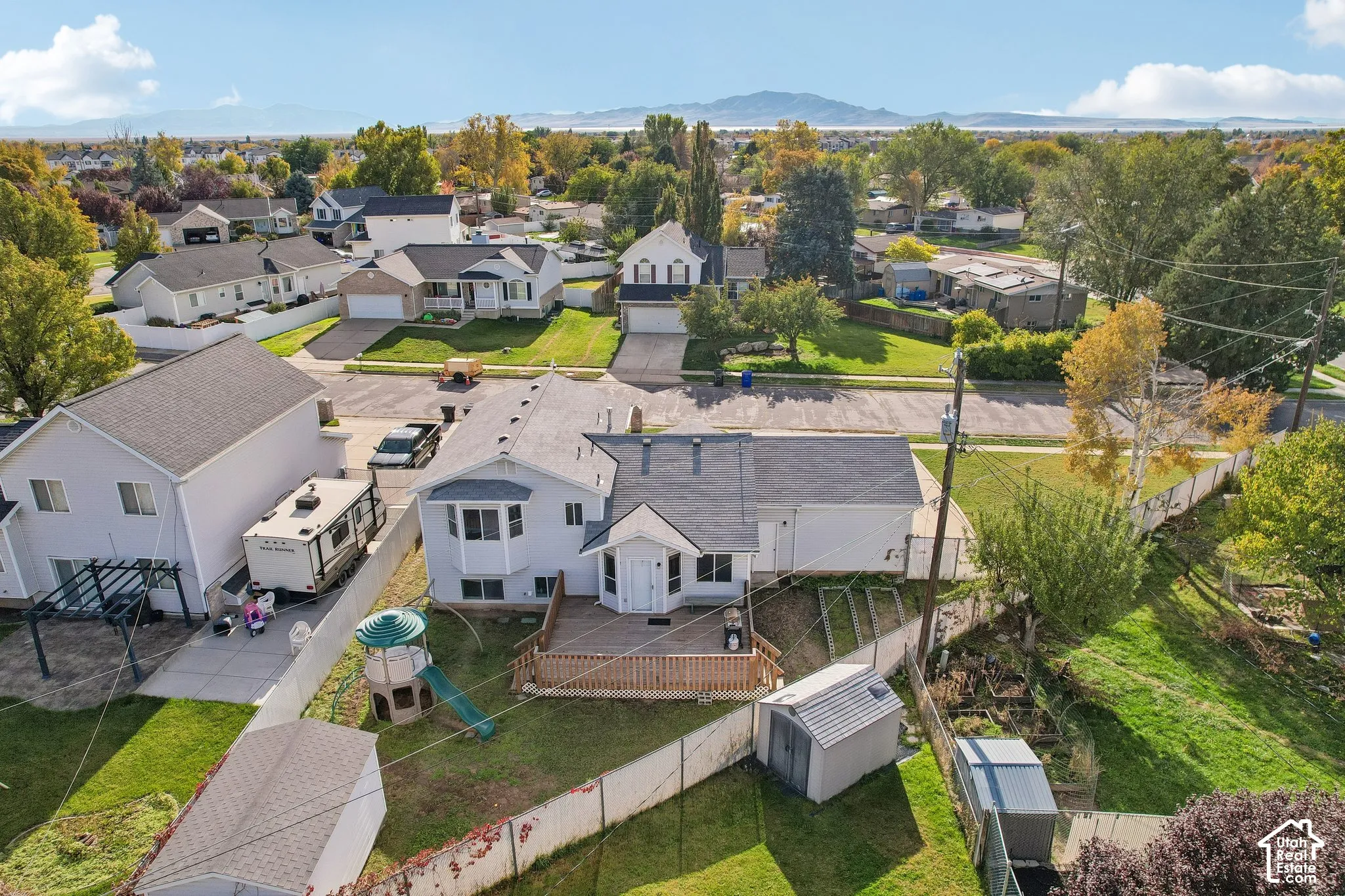 Aerial perspective of a detached residence featuring a wood-decked patio, chain-link perimeter fencing, and a mountain range backdrop