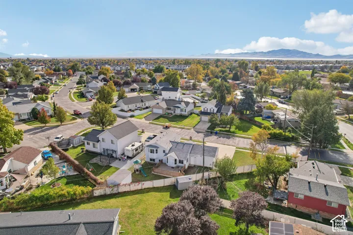 Aerial perspective featuring a multi-level suburban residence, a fenced-in rear yard with a wooden deck, and a prominent mountain range backdrop