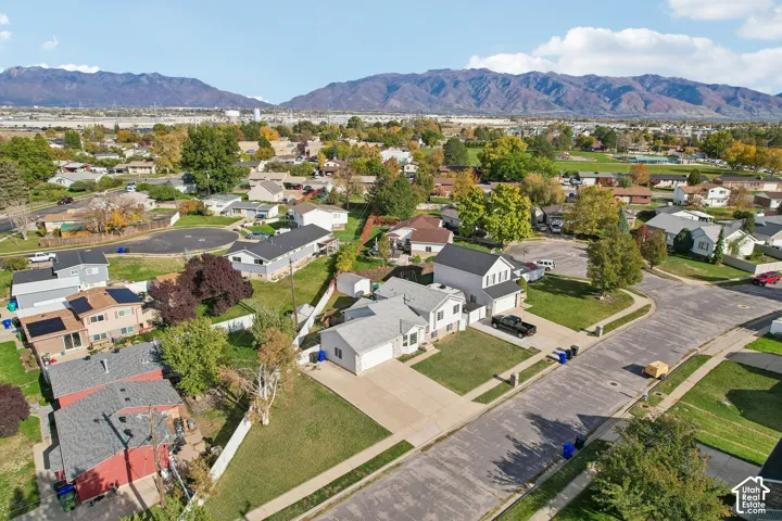 Aerial view of a residential property featuring an attached garage, a concrete driveway, a front lawn, and mountain scenery