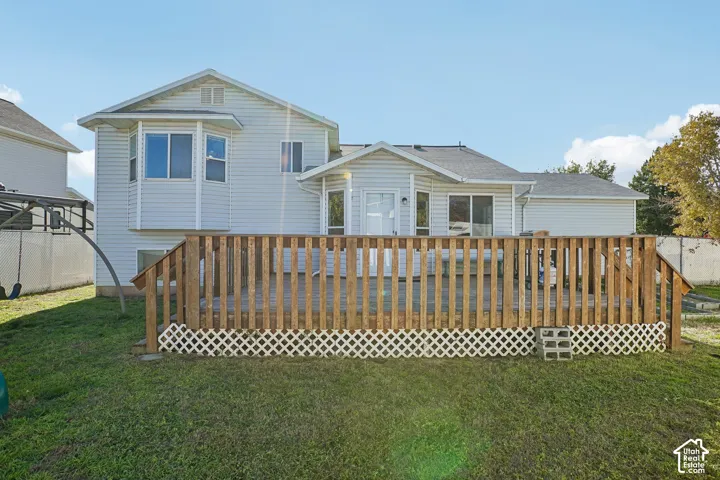 Rear exterior featuring light-colored horizontal siding, a two-story bay window structure, and a wood deck with lattice skirting