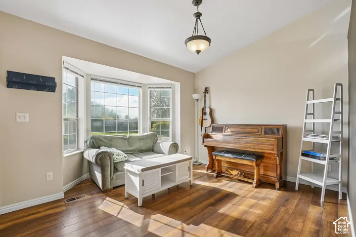 Living space featuring wood-finish flooring, vaulted ceilings, a multi-pane bay window, and a hanging pendant light fixture