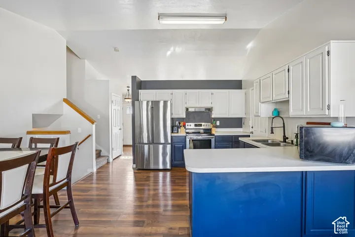 Kitchen featuring white upper cabinetry, blue lower cabinetry, stainless steel appliances, a peninsula with a solid-surface countertop, and wood-finish flooring