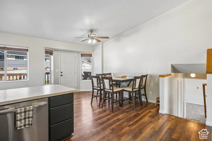 Open-concept area featuring wood-finish flooring, a ceiling fan with integrated lighting, dual-tone cabinetry, and a kitchen island with a neutral countertop