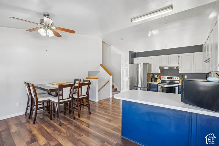 Kitchen featuring white upper cabinetry, blue lower cabinetry, stainless steel appliances, and a breakfast bar, complemented by wood-finish flooring and a ceiling fan