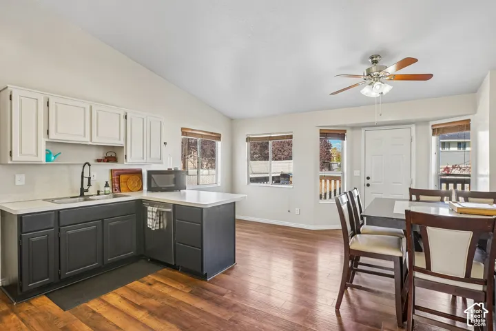 Two-toned cabinetry with light upper and dark lower units, wood-finish flooring, vaulted ceilings, multi-pane windows, and a ceiling fan with integrated lighting