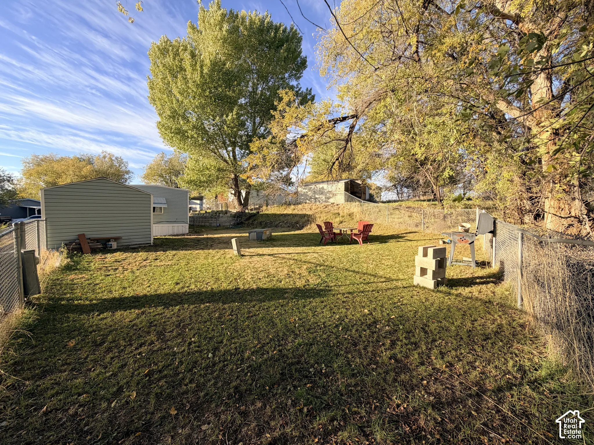 Fenced backyard featuring mature trees, a detached storage structure, and a retaining wall