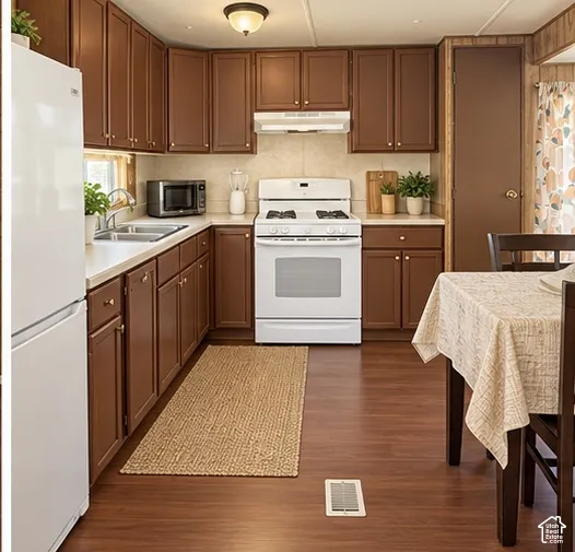 Kitchen featuring shaker-style wood cabinetry, white appliances, solid surface countertops, a stainless steel double-basin sink, and wood-finish flooring
