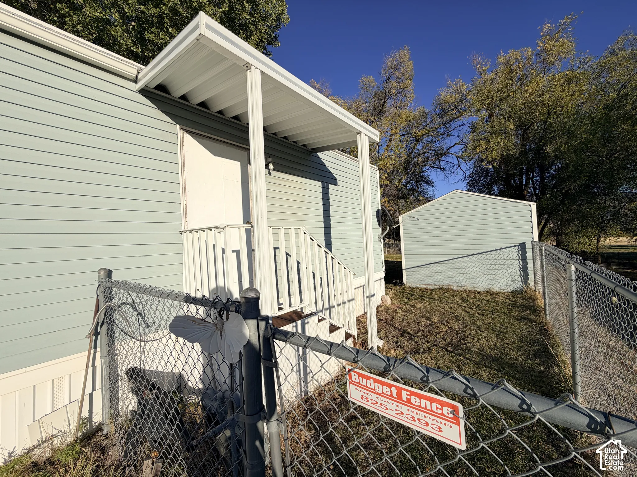 Exterior featuring horizontal siding, a covered entry with a metal overhang, an attached staircase, and a detached exterior storage structure enclosed by chain-link fencing