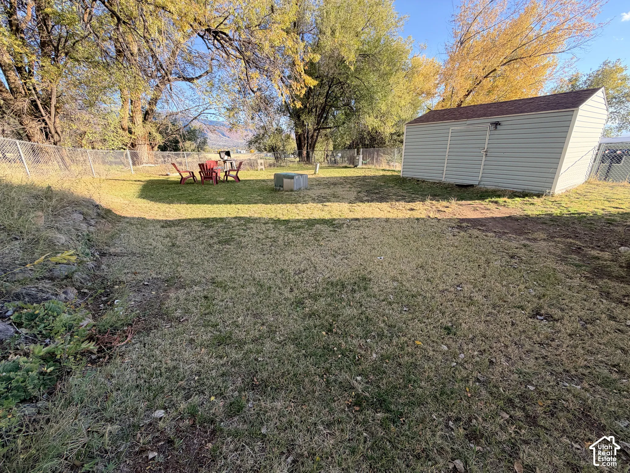 Spacious backyard featuring a storage shed, chain-link fencing, mature trees, and mountainous terrain in the distance