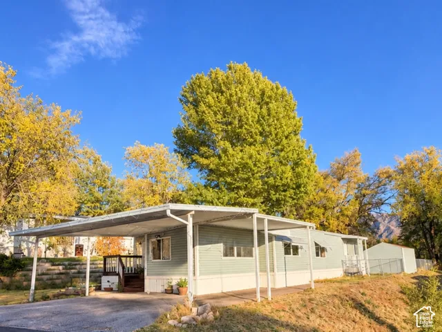 Exterior featuring horizontal light green siding, covered carport, wooden deck, and a detached storage shed