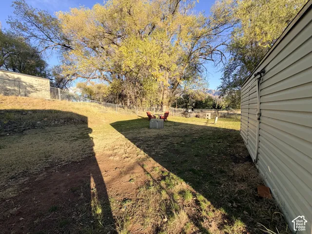 Expansive yard space featuring mature trees, perimeter chain-link fencing, and horizontal vinyl siding
