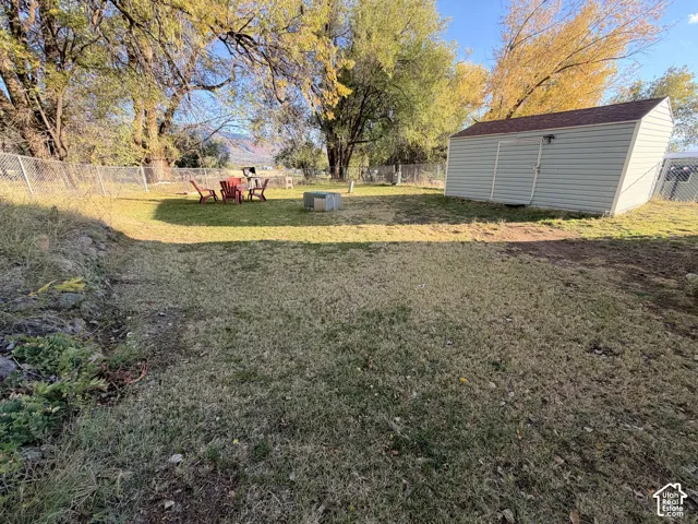 Spacious backyard featuring a storage shed, chain-link fencing, mature trees, and mountainous terrain in the distance