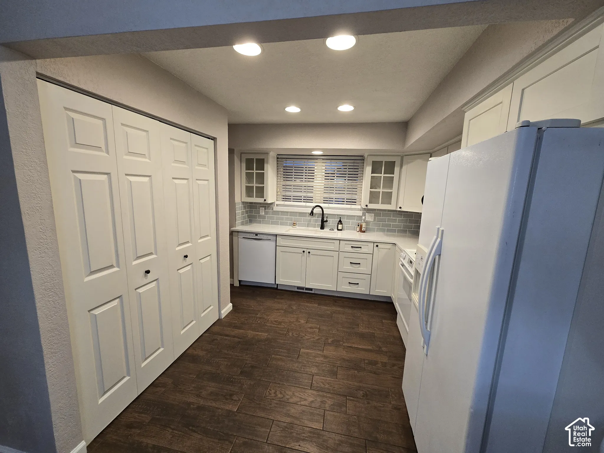 Kitchen featuring wood-finish flooring, white shaker-style cabinetry with glass-panel upper doors, subway tile backsplash, and recessed lighting