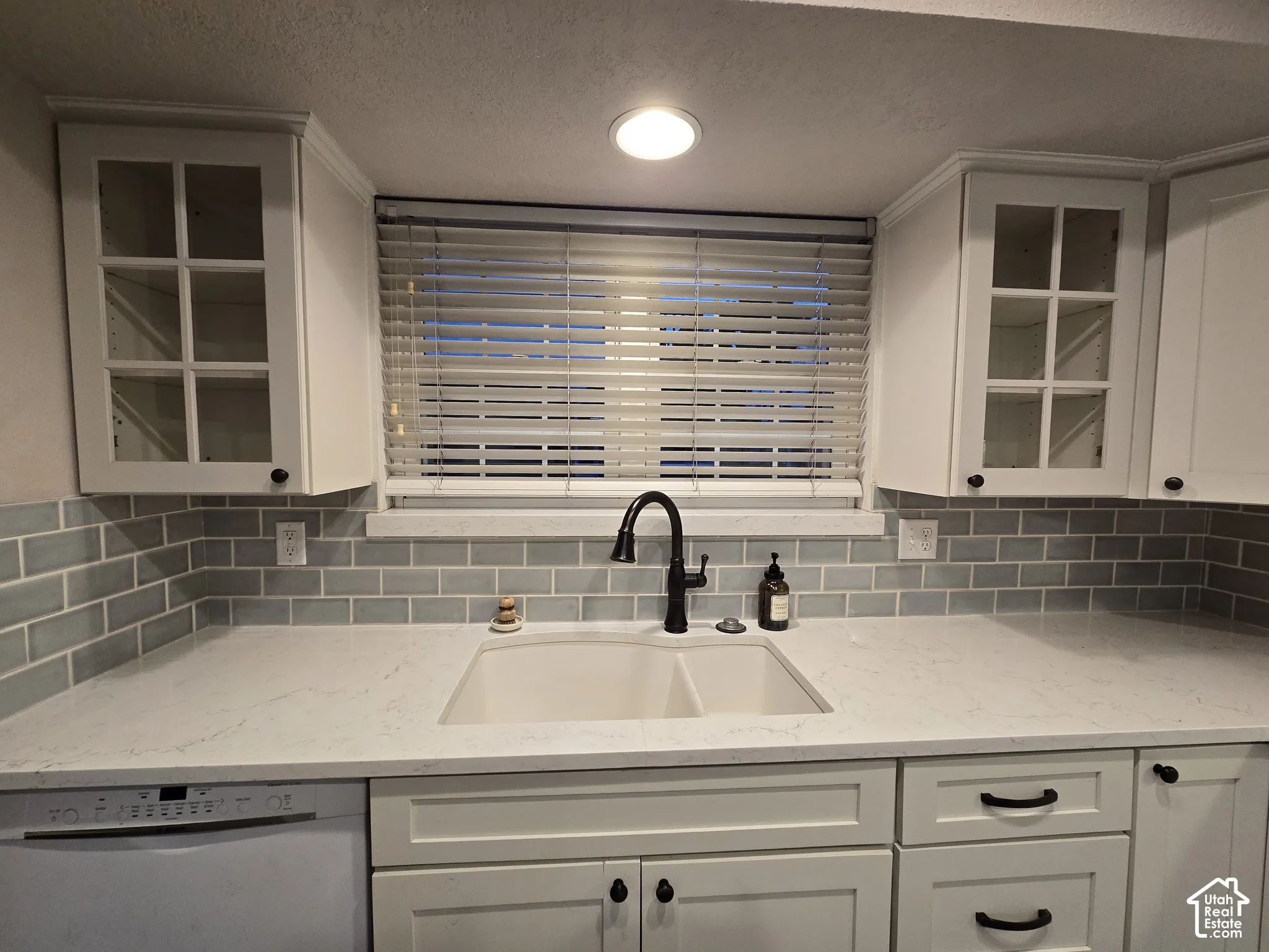 Kitchen featuring white cabinetry with glass-panel upper doors, solid-surface countertops, a matte black arched faucet with a dual-basin undermount sink, and a light blue subway tile backsplash