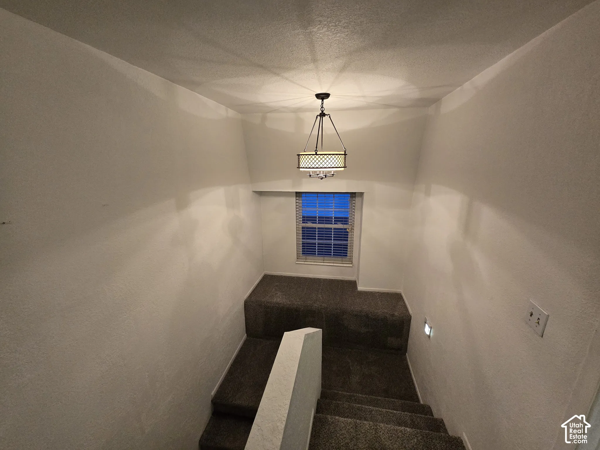 Stairwell featuring carpeted steps and landing, a multi-light drum chandelier, and a recessed window with paneled blinds