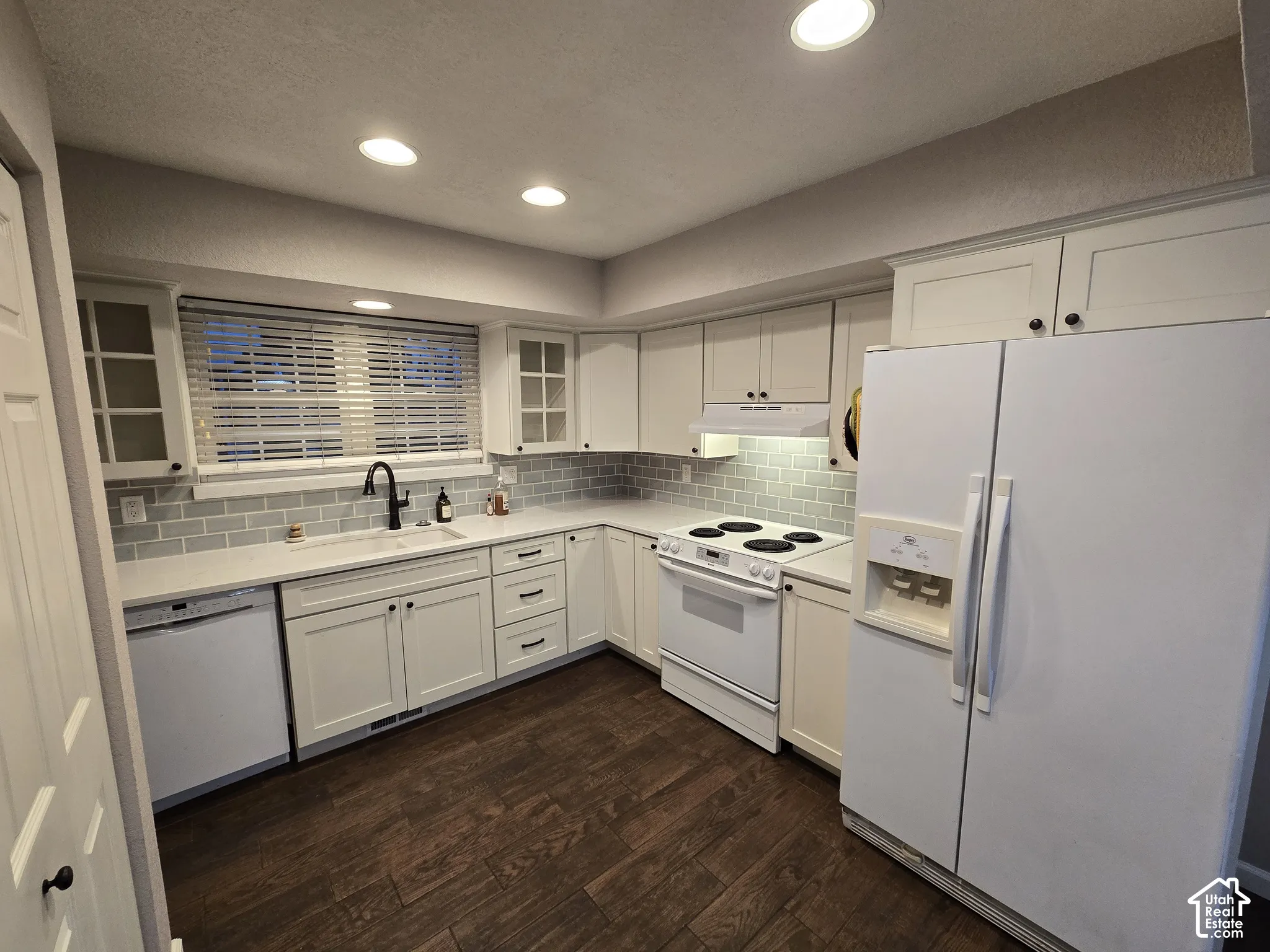 Kitchen featuring white cabinetry, subway tile backsplash, solid-surface countertops, wood-finish flooring, and recessed lighting