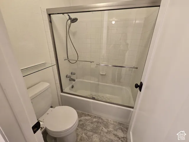 Bathtub and shower combination with floor-to-ceiling tile surround, glass sliding enclosure, adjustable handheld shower head, and stone-finish tile flooring