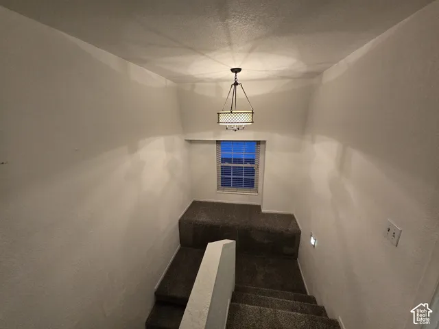 Stairwell featuring carpeted steps and landing, a multi-light drum chandelier, and a recessed window with paneled blinds