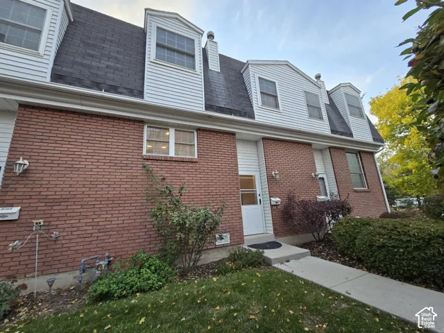 Multi-level exterior featuring red brick masonry, white horizontal siding, steep-sloped roofline with dormer windows, and a concrete walkway