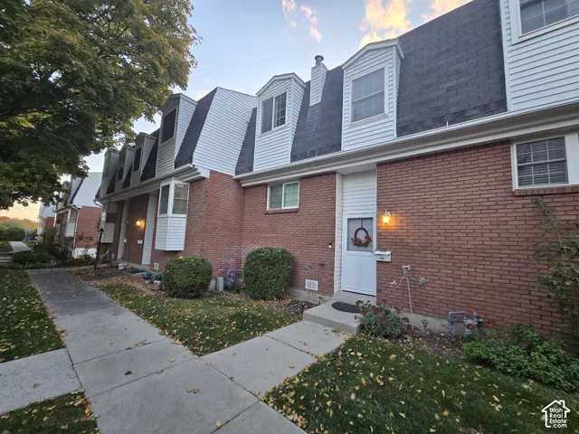 Exterior featuring red brick masonry, white siding, mansard rooflines, dormer windows, and a paved concrete walkway
