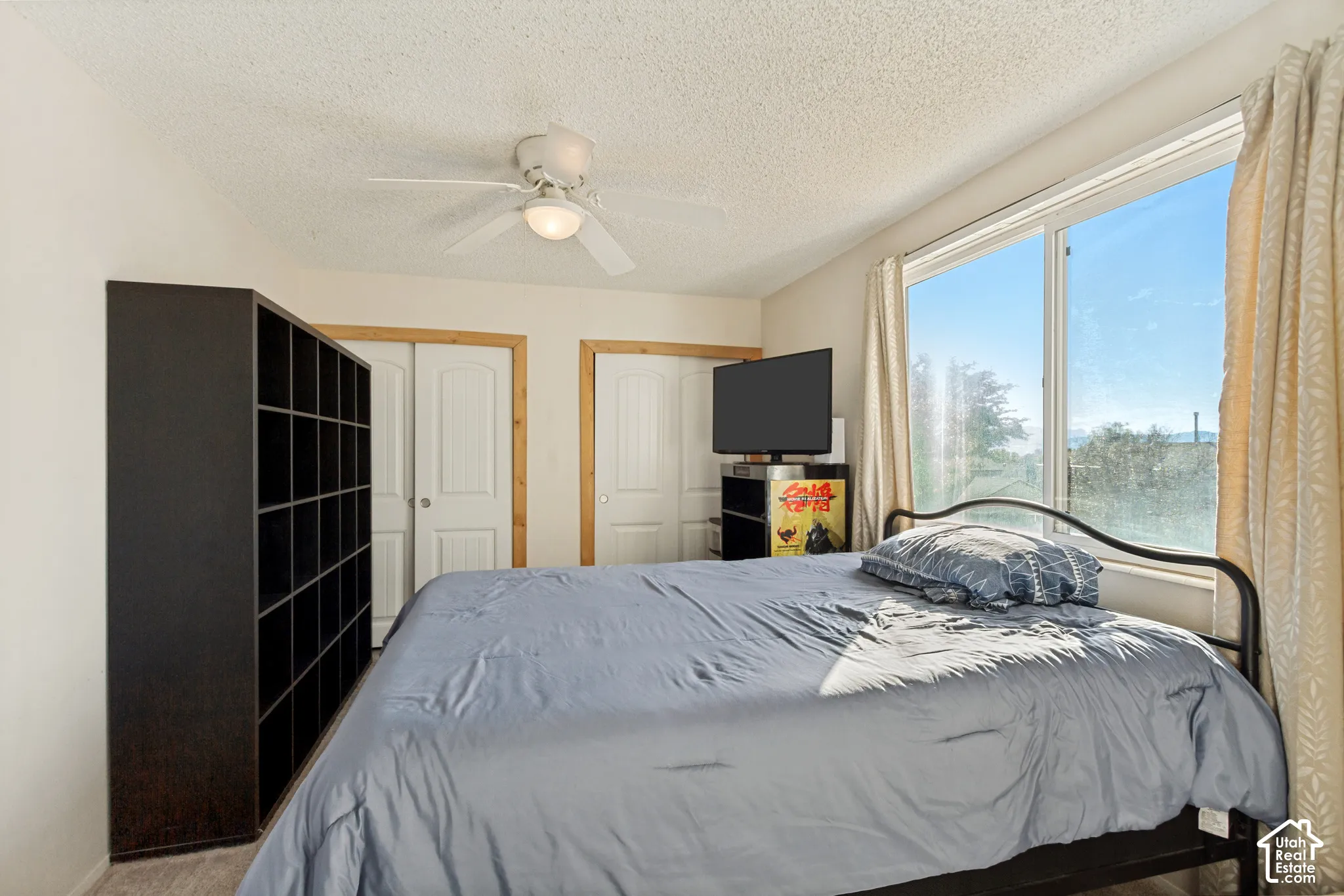 Room featuring a large window, dual closets with wood trim, and a ceiling fan with integrated lighting