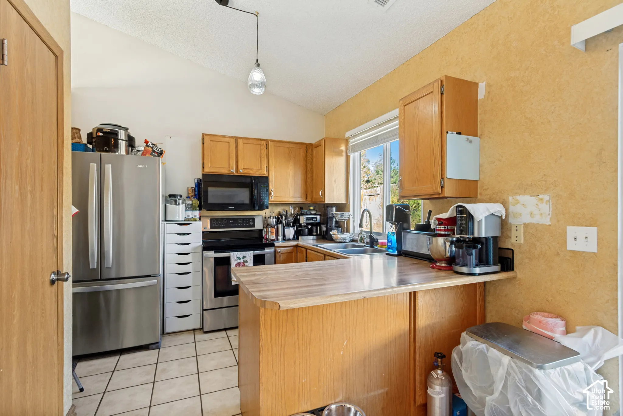 Kitchen featuring vaulted ceilings, wood cabinetry, stainless steel appliances, a peninsula counter, and ceramic tile flooring