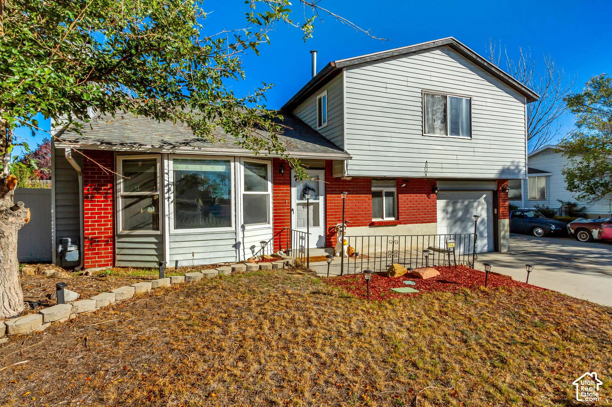 Multi-level exterior featuring a combination of brick and horizontal siding, a bay window, a metal-railed front porch, and an attached garage