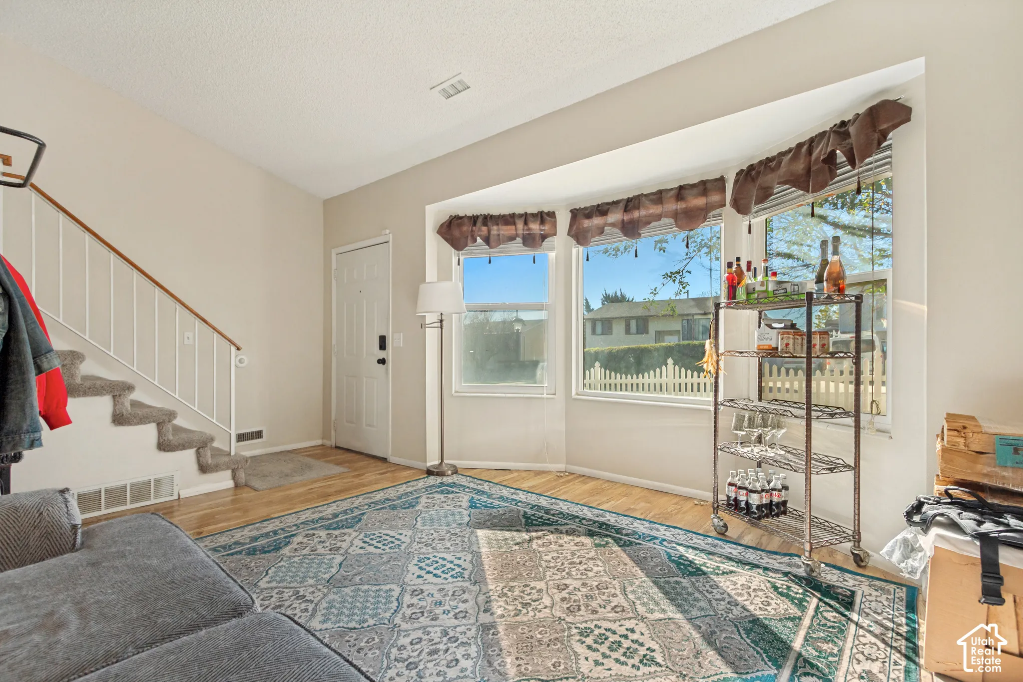 Vaulted ceilings, expansive bay windows, wood-finish flooring, and a staircase featuring a white metal railing