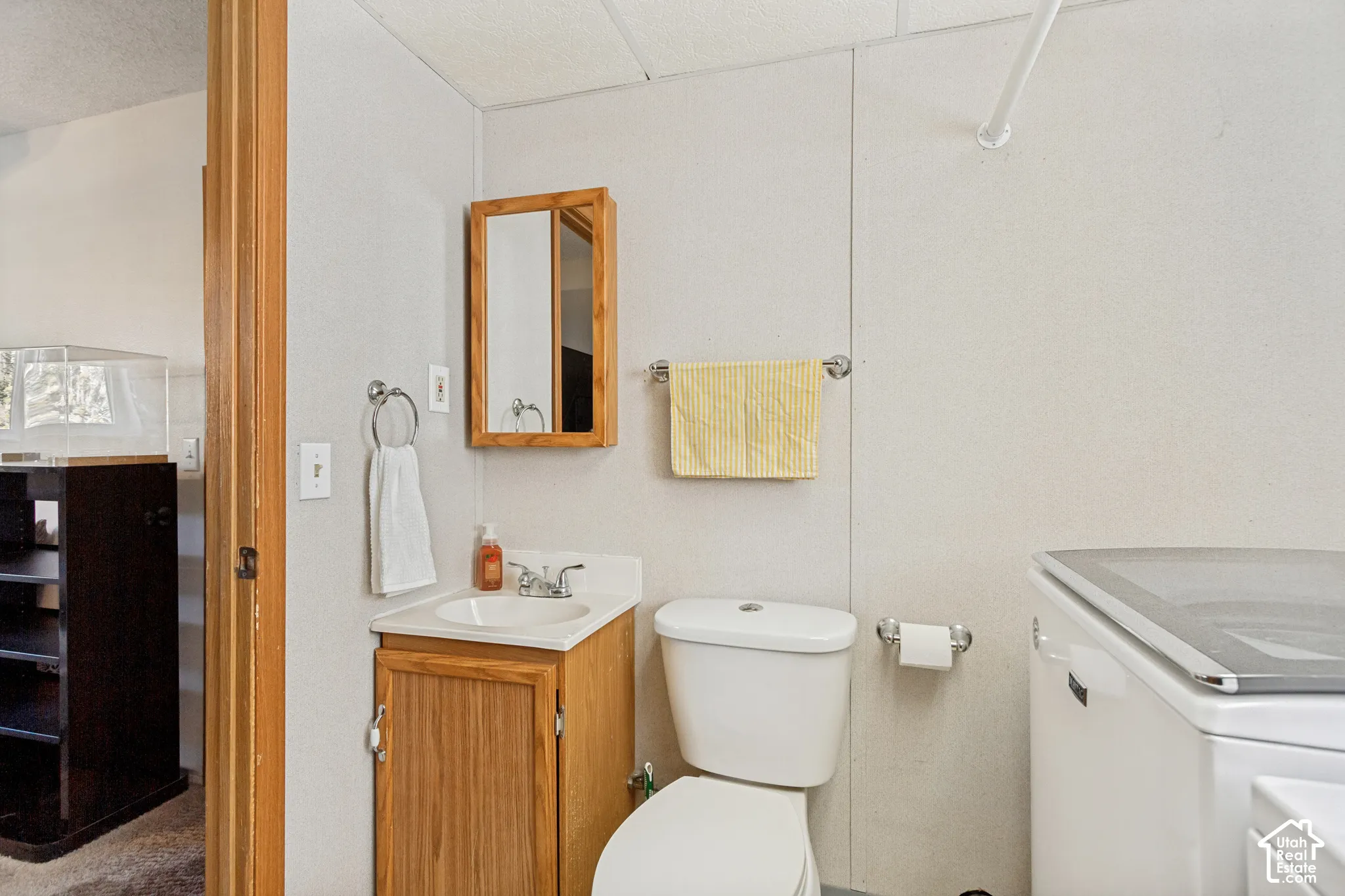 Bathroom featuring a wood-finish vanity with a drop-in basin, surface-mounted medicine cabinet, white toilet, and chrome-finish hardware