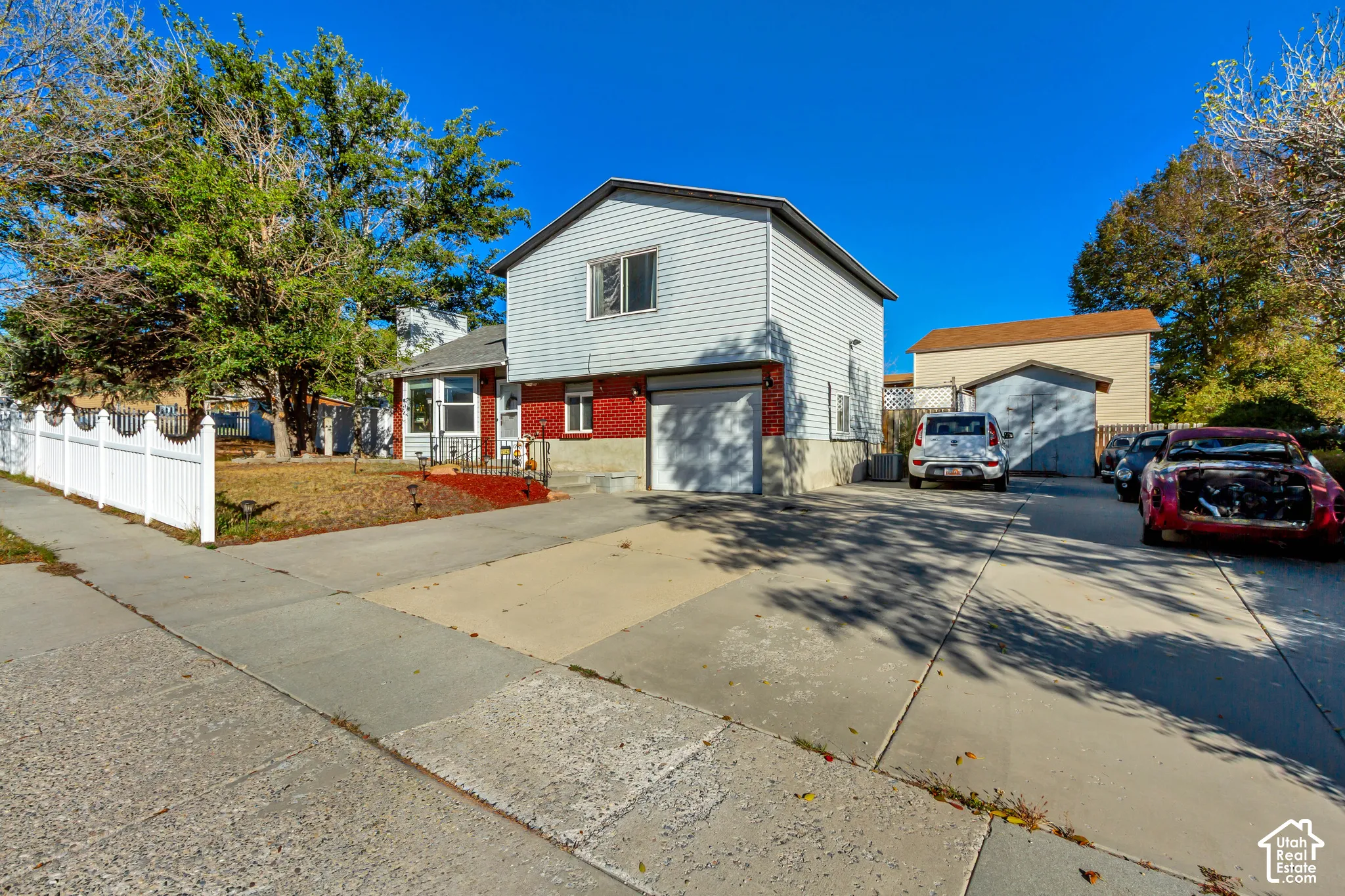 Two-story exterior featuring light-colored horizontal siding, brick masonry, an attached garage, and a white privacy fence