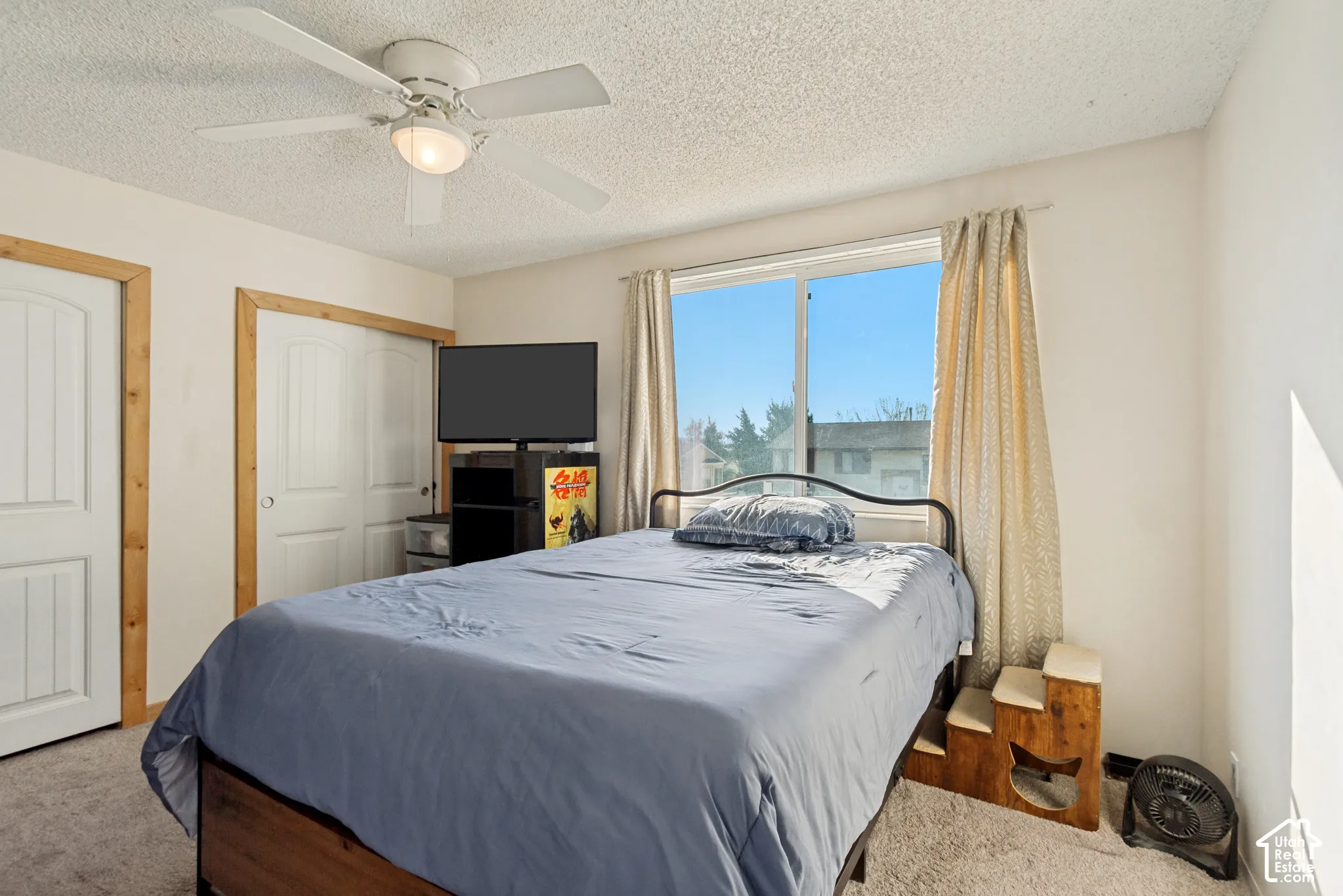 Room featuring neutral wall-to-wall carpeting, a ceiling fan with integrated lighting, dual-panel interior doors with natural wood trim, and a sliding window