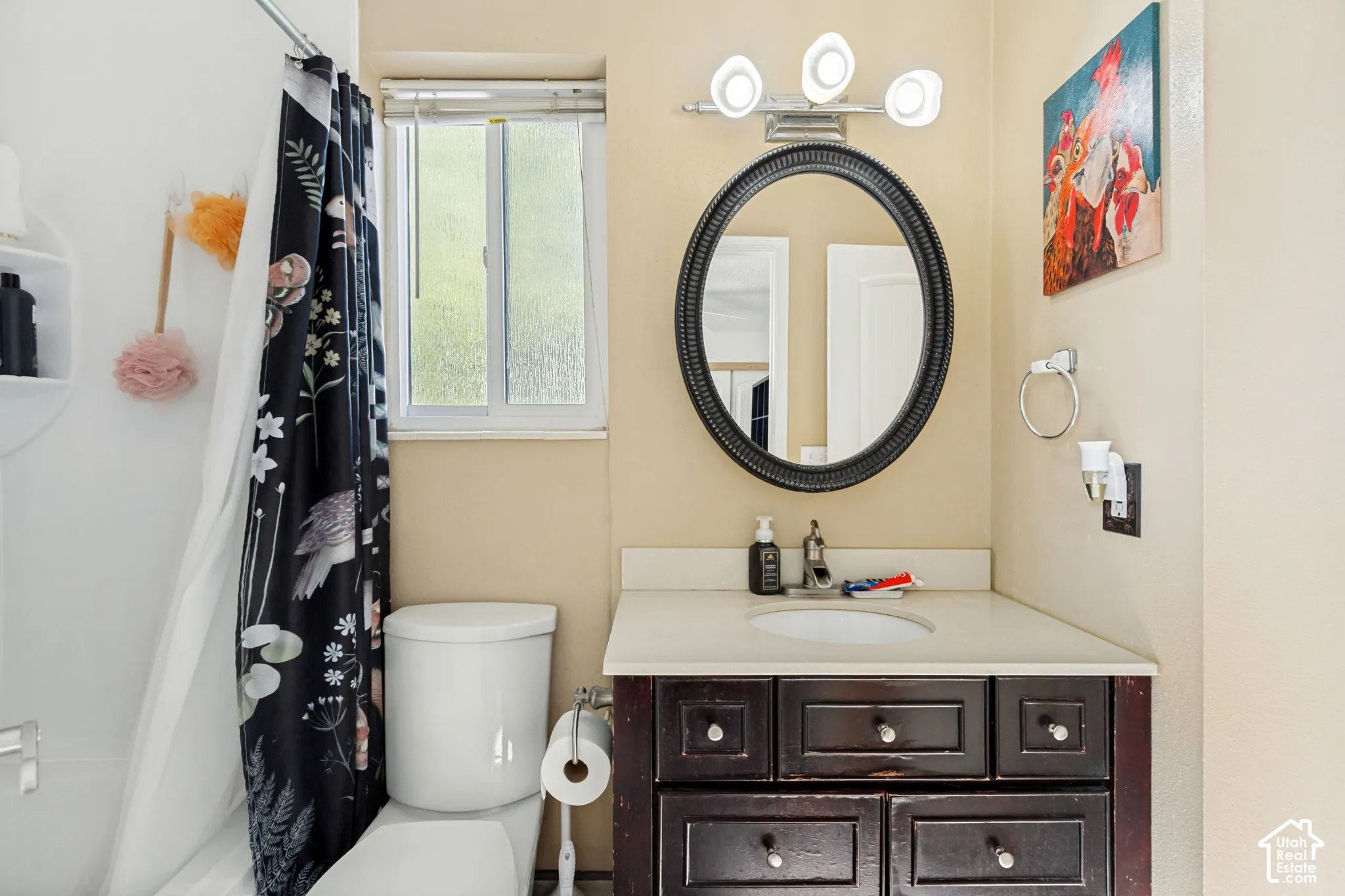 Bathroom featuring a dark-finish wood vanity, neutral countertop with an integrated sink, oval mirror, three-light fixture, and a sliding window
