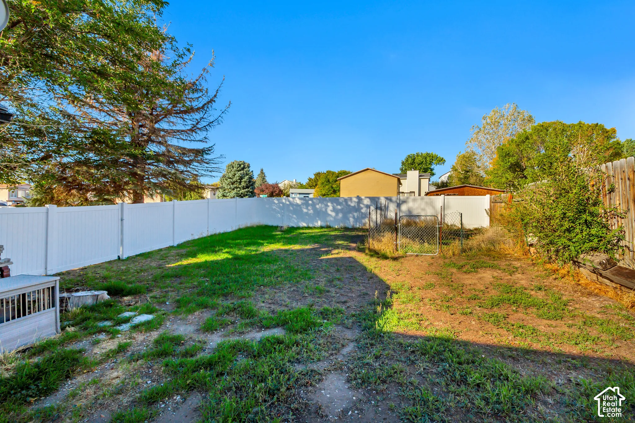Backyard featuring a white vinyl privacy fence, mature trees, and a chain-link enclosure