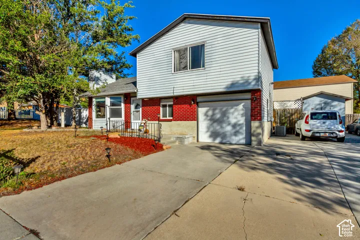 Split-level exterior featuring brick and horizontal siding, an attached single-car garage, and an expansive concrete driveway