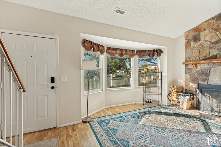 Living space featuring a floor-to-ceiling multi-tone stone fireplace with a wood mantel, wood-finish flooring, and a three-pane bay window