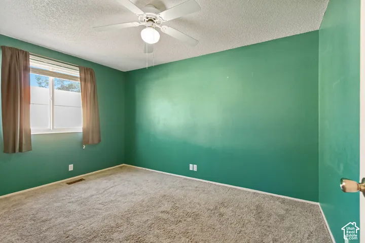 Room featuring textured ceiling, neutral carpeting, sliding window, and a central ceiling fan with integrated lighting