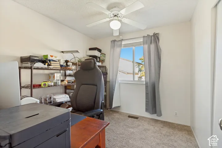 Neutral-toned bedroom featuring carpeted flooring, a white ceiling fan with integrated lighting, and a sliding window