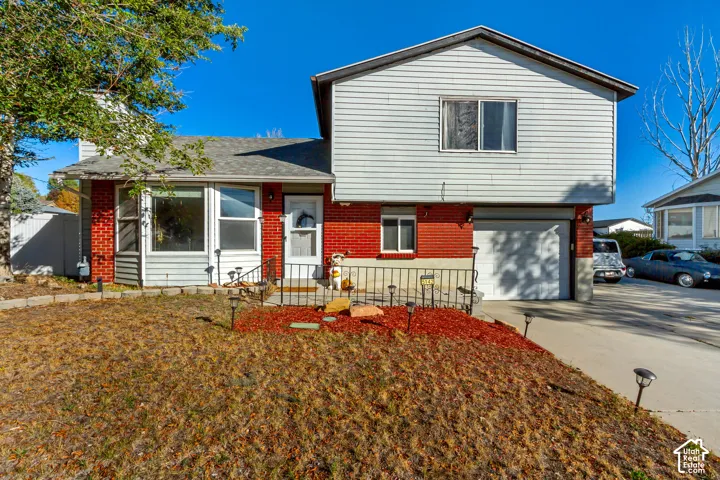 Multi-level exterior featuring a red brick and horizontal siding facade, an attached garage, and a concrete driveway
