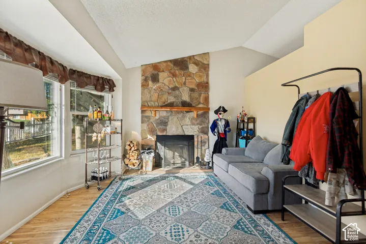 Vaulted ceiling, floor-to-ceiling stone fireplace, wood-finish flooring, and multi-pane bay windows