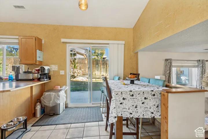 Kitchen area featuring a peninsula, wood cabinetry, tile flooring, vaulted ceiling, and sliding glass patio door