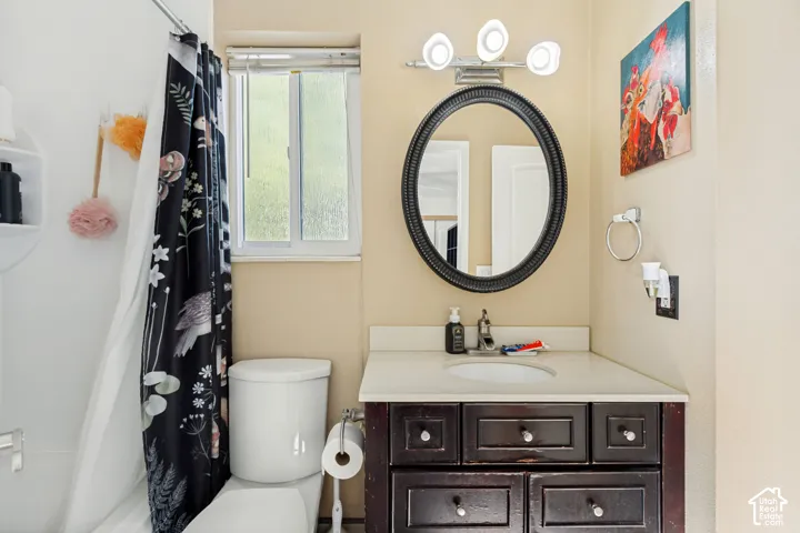 Bathroom featuring a dark-finish wood vanity, neutral countertop with an integrated sink, oval mirror, three-light fixture, and a sliding window